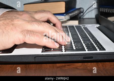 Ein Mann arbeitet an einem Computer, seine Hände sind auf der Laptop-Tastatur. Stockfoto
