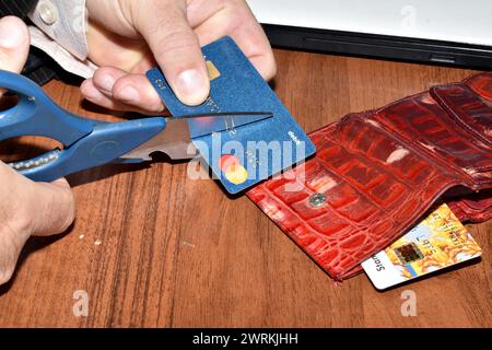 Das Bild zeigt männliche Hände, die eine Schere und eine Plastikkarte halten. Der Mann zerstört die Karte mit einer Schere. Stockfoto