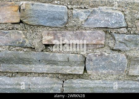 Ein detaillierter Blick auf die vielfältigen Texturen und Farben von alten Steinen in einer Wand, die bei Tageslicht erfasst werden. Stockfoto