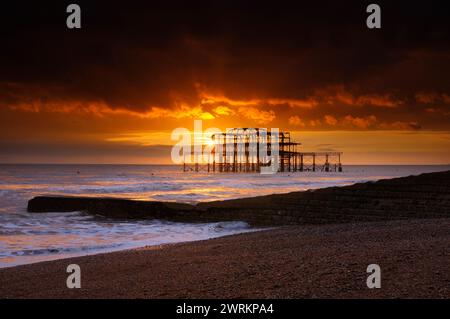 Ein wunderschöner orangener Sonnenuntergang hinter den Ruinen des Brighton West Pier im Meer von der Schindelküste von Brighton Beach, Brighton and Hove, East Sussex, UK 2024 Stockfoto