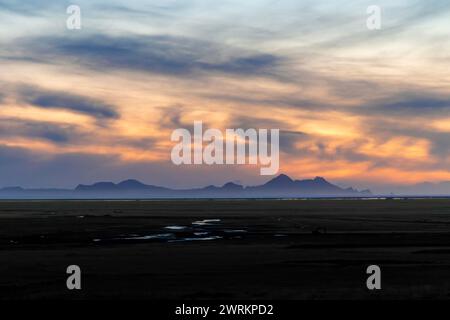 Ein wunderschöner Sonnenuntergang über einer weiten, leeren Ebene. Der Himmel ist voller Wolken, und die Sonne geht hinter den Bergen unter. Die Szene ist friedlich und ruhig. Stockfoto