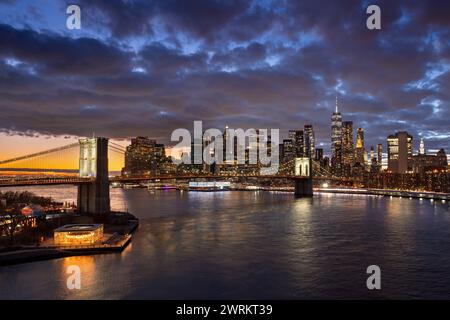 Brooklyn Bridge und Uferpromenade mit dem East River. Dumbo und Lower Manhattan beleuchtete Wolkenkratzer in der Dämmerung, New York City Stockfoto
