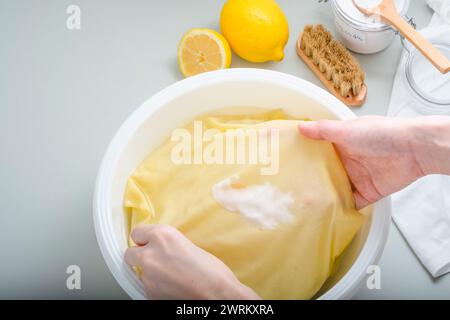 Nicht erkennbare Person Hand hält schmutzigen, scharfen Soßenfleck auf einem gelben Hemd. Natürliche Reinigungsmittel. Daily Life Flin Concept. Draufsicht. Stockfoto