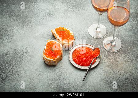 Kleine Metallplatte mit rotem Lachskaviar, zwei Kaviar Toast Canape, zwei Gläser Champagner von oben auf grauem Betonhintergrund, festlicher Luxus Stockfoto
