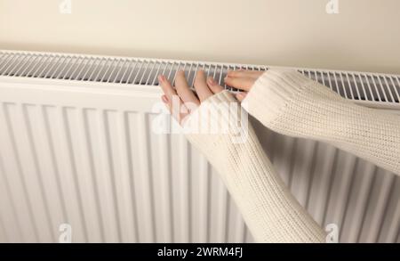 Eine Frau wärmt ihre Hände auf dem Heizkörper der Zentralheizung des Hauses, Nahaufnahme, Stockfoto
