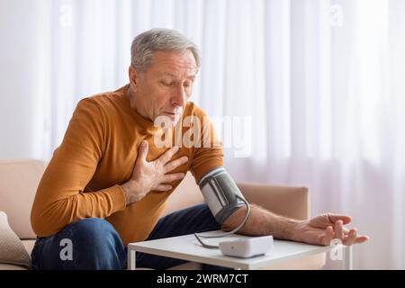 Seniorenmann Fühlt Sich Zu Hause Unwohl, Kontrolliert Den Blutdruck Stockfoto