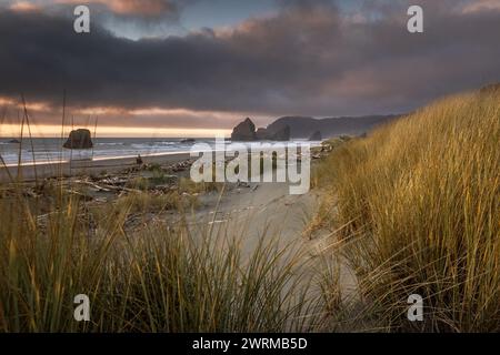 Ein Strand mit einer felsigen Küste und einer Grasfläche. Der Himmel ist bewölkt und die Sonne untergeht Stockfoto