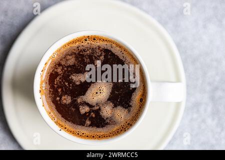 Blick von oben auf eine dampfende, frisch gebrühte Tasse Kaffee in einer weißen Tasse, die auf einer passenden Untertasse auf einer strukturierten Oberfläche platziert wird. Stockfoto