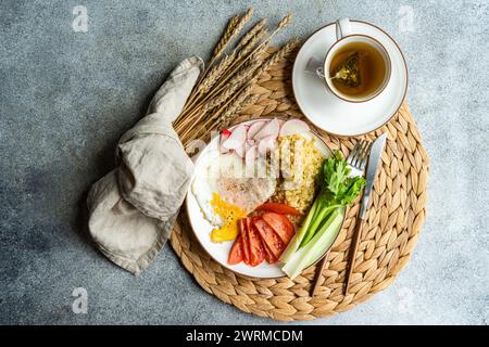 Ein ausgewogenes Mittagessen mit frischen Radieschen, Tomaten, Sellerie, Spiegelei und Bulgur-Müsli, begleitet von einer warmen Tasse Tee, präsentiert auf einer wicke Stockfoto