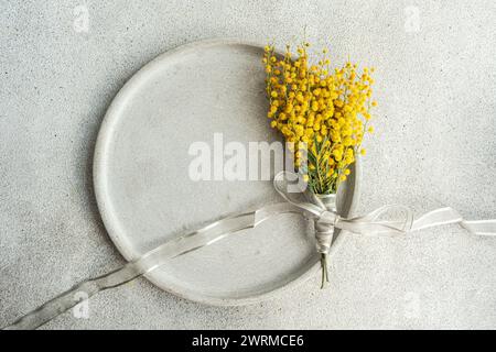 Blick von oben auf das zarte Arrangement von leuchtenden Mimosa-Blüten, die mit einem silbernen Band gebunden sind, präsentiert auf einer eleganten, strukturierten Tischoberfläche für einen eleganten Look Stockfoto