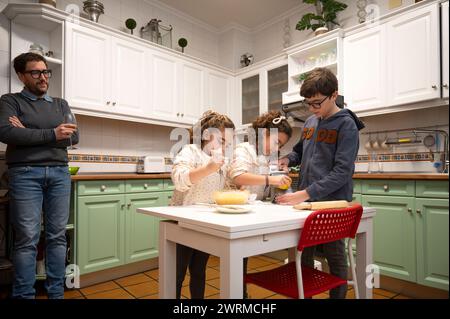 Familie genießt Zeit zusammen in der Küche, mit Kindern backen und ein Erwachsener beaufsichtigt. Stockfoto