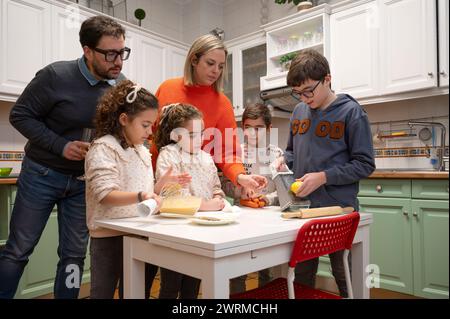 In der Küche versammelt sich eine generationenübergreifende Familie, die gemeinsam eine Mahlzeit zubereitet, wobei Kinder und Erwachsene aktiv beteiligt sind. Stockfoto