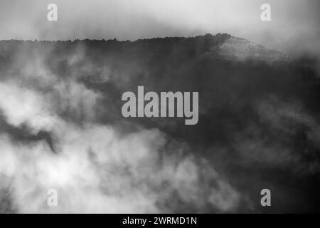 Ein Schwarzweiß-Bild, das einen Berggipfel einfängt, der kaum durch eine dichte Nebeldecke sichtbar ist. Stockfoto