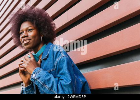 Eine strahlende junge Frau lächelt, Kopfhörer um den Hals, vor einem geometrischen Hintergrund, verkörpert urbane Kühle Stockfoto