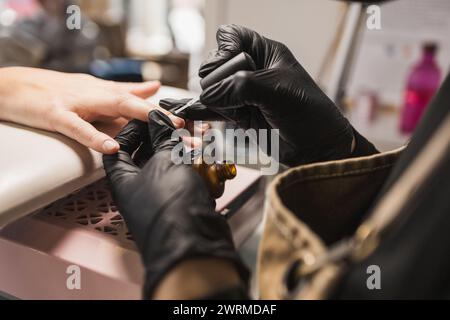 Eine detaillierte Nahaufnahme eines professionellen Manikürers, der während einer Nagelpflege in einem Salon Öl auf die Nagelhaut eines Kunden aufträgt Stockfoto