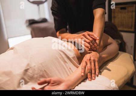 Eine professionelle Masseurin bietet eine entspannende Massage für einen Kunden, der auf einem Massagetisch liegt und sich auf die Hände konzentriert Stockfoto