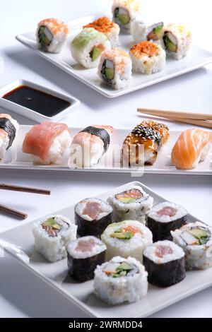 Eine verlockende Auswahl an Sushi-Brötchen, die ordentlich auf zwei weißen Tellern angeordnet sind, begleitet von Sojasauce und Essstäbchen. Stockfoto