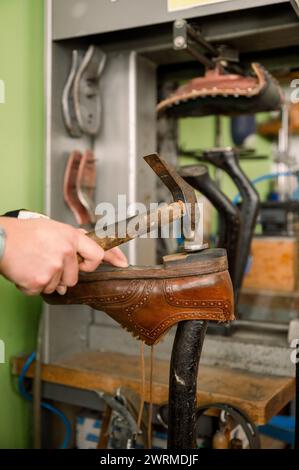 Eine abgeschnittene, nicht erkennbare Handwerkerhand, die in einer Schuhmacherwerkstatt in Österreich auf eine Schuhsohle hämmert, zeigt die Kunst der traditionellen Schuhherstellung. Stockfoto