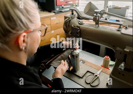 In einer gut ausgestatteten Werkstatt in Österreich näht ein nicht erkennbarer Schuhmacher mit einer Nähmaschine Leder akribisch und zeigt handwerkliche Handwerkskunst Stockfoto