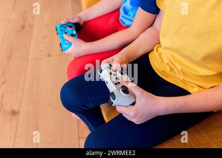 Zugeschnittenes Bild von zwei Kindern, die mit farbenfrohen Controllern spielen und sich auf ihre Hände und Geräte konzentrieren Stockfoto