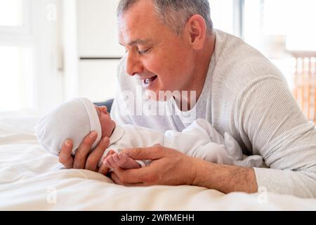Ein liebenswerter Moment, in dem ein verspielter Vater mit seinem aufmerksamen neugeborenen Baby interagiert und beide eine warme Familienverbindung genießen Stockfoto
