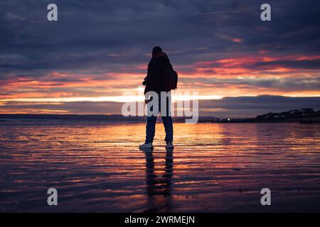 Erkunden Sie den Mann an einem Strand in Großbritannien bei einem wunderschönen Frühlingssonnenuntergang. Stockfoto