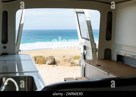 Erleben Sie Ruhe durch die offene Rückseite eines Vintage-Minibusses mit Blick auf eine ruhige Strandszene. Stockfoto