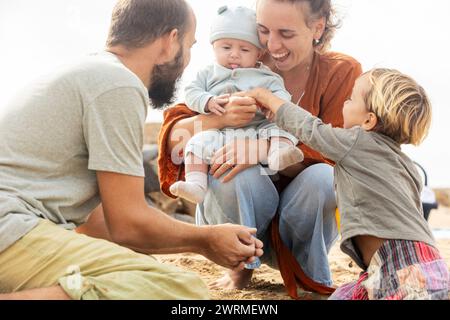 Eine glückliche Familie genießt eine schöne Zeit am Strand, während ein Kleinkind ein verspieltes Baby erreicht. Stockfoto