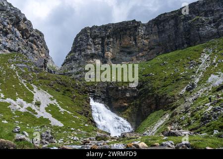 Ein mächtiger Wasserfall stürzt einen felsigen Bergpass hinunter, eingerahmt von grünen Hängen im Valle de Ordesa, Huesca Stockfoto