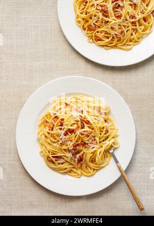 Blick von oben auf klassische Spaghetti Carbonara, garniert mit Käse und Speckstücken, serviert auf weißen Tellern mit rustikalem Hintergrund. Stockfoto