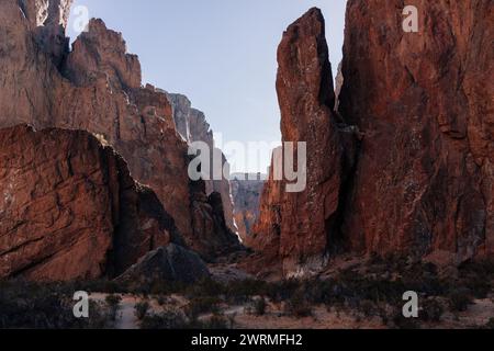 Ein schmaler Pfad schlängelt sich durch hoch aufragende rote Klippen unter klarem Himmel in der zerklüfteten und abgelegenen Landschaft Patagoniens, Argentinien Stockfoto