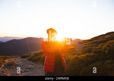 Ein Fotograf mit Silhouetten macht Fotos bei Sonnenaufgang mit einer DSLR in den ruhigen Bergen. Stockfoto