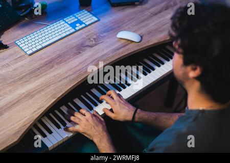 Nicht erkennbarer männlicher Musiker, der während einer intimen Heimklang-Studioaufzeichnung ein digitales Klavier spielt, mit Studioausstattung im Hintergrund. Stockfoto