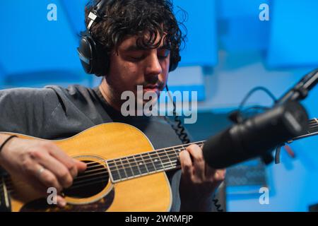 Ein Künstler konzentrierte sich auf das Spielen einer Akustikgitarre während einer Tonstudioaufnahmesitzung mit einem Mikrofon vorne. Stockfoto