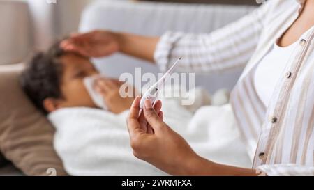 Schwarze Mutter berührt die Stirn des Sohnes und überprüft seine Temperatur mit einem Digitalthermometer Stockfoto