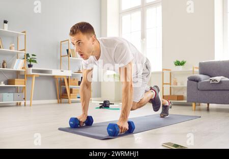Motivierter Mann, der eine Plank-Übung mit Kniestrücken während eines Fitness-Workouts zu Hause macht Stockfoto