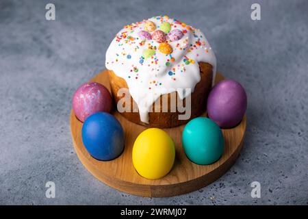 Osterkulich mit kandierten Früchten in weißer Glasur mit bunten Streuseln und bemalten Eiern. Traditionelles Ostergebäck. Osterferien. Nahaufnahme, wählen Sie Stockfoto