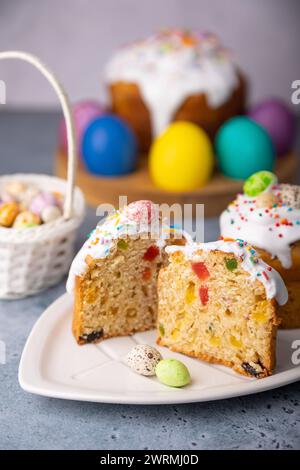 Zwei kleine Osterkulichs mit kandierten Früchten in weißer Glasur mit bunten Streuseln im Schnitt. Bemaltes Hühnchen und Wachteleier. Traditionelle Osterbak Stockfoto