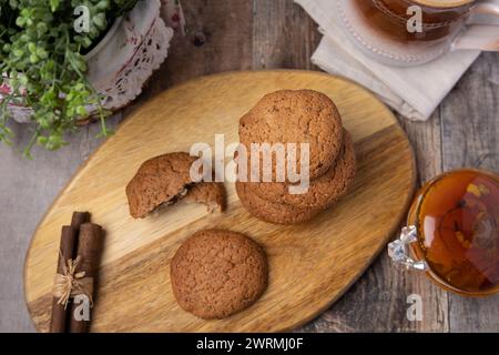 Haferflocken-Rosinenkekse auf einem Holzbrett mit Zimtstangen und einer Tasse Milch. Traditionelles hausgemachtes Gebäck im rustikalen Stil. Selektiver Fokus Stockfoto