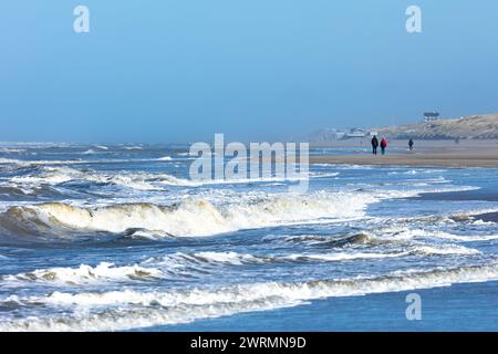 Egmond aan Zee, Niederlande - 17. März 2022: Wellen in der rauen Nordsee mit einigen Menschen, die in der Sonne am Ufer entlang laufen Stockfoto