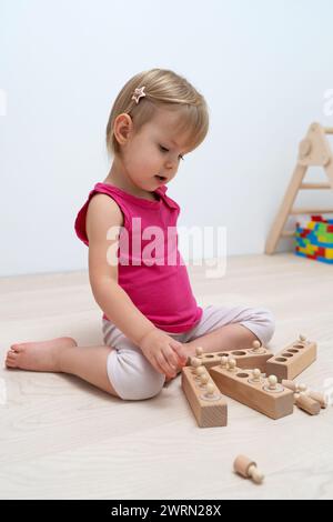 Ein 2,5-jähriges Kind sortiert Formen unterschiedlicher Größe. Holz-Kinderspiel nach Montessori-System. Hölzerne Noppzylinder für Vorschulspiele Stockfoto