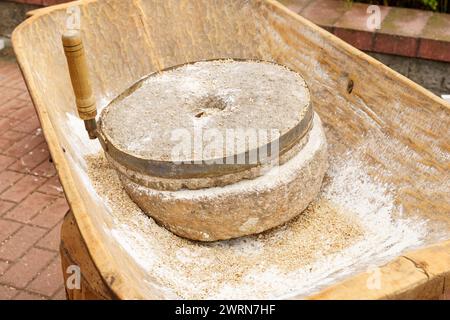 Eine Nahaufnahme einer altmodischen Steinmühle, die zum Mahlen von Körnern verwendet wurde, auf einem Holztisch mit Mehlrückständen positioniert. Stockfoto