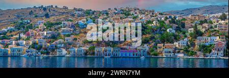 Blick auf die Insel Symi von Griechenland, mit farbenfrohen neoklassizistischen Villen, die die Hänge in der Nähe der Hauptstadt bedecken. Teil der Dodekanesischen Inselkette. Schwester Stockfoto