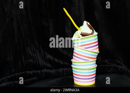 Bunte gestreifte Tasse mit cremigem Schokoladeneis und gelbem Löffel auf dunklem strukturiertem Hintergrund Stockfoto