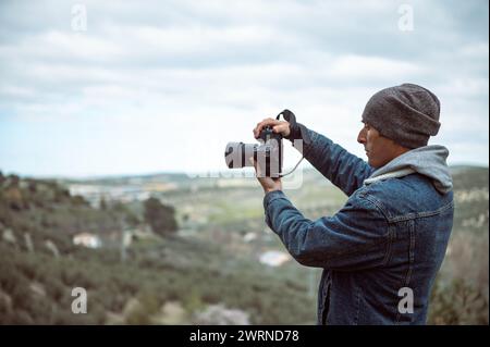 Mann Fotograf, der mit einer professionellen Kamera einen wunderschönen Blick auf die Berge aufnimmt. Hübscher junger Erwachsener in lässigem Denim, mit Kamera, fotografiert Stockfoto