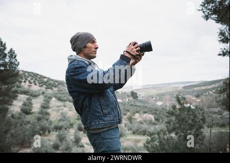 Junger Reisender Fotograf Mann, Wanderer in lässigem Denim, blickt in die Ferne und macht Fotos von Bergen mit einer professionellen Digitalkamera Stockfoto