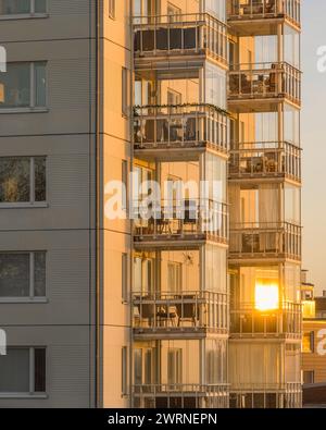 Ein hohes Wohngebäude in Göteborg, Schweden, mit zahlreichen Balkonen. Das Gebäude wird von den warmen Farbtönen des Sonnenaufgangs beleuchtet, wodurch ein Stockfoto