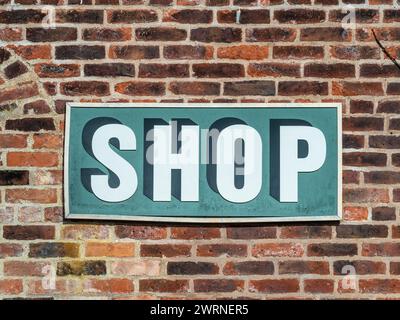 Ein hölzernes Schild an einer Ziegelwand, auf dem das Wort „Shop“ handbemalt ist. Stockfoto