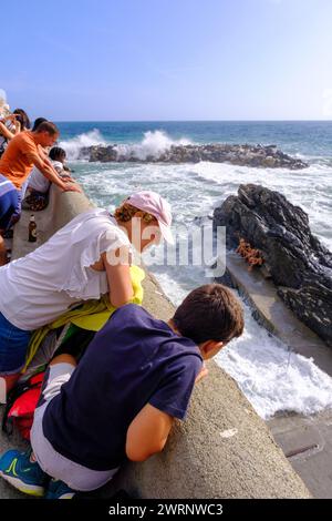 Manarola, IT - 25. Juli 2023: Menschen, die große Wellen beobachten, die auf den Felsen krachen Stockfoto
