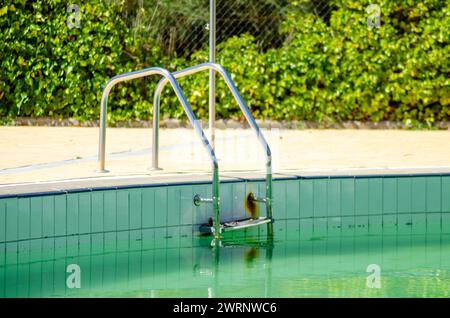 Metallleitern in einem Schwimmbad mit schmutzigem Wasser Stockfoto
